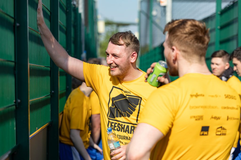 Charity football tournament players have a chat on the sidelines in yellow Lifeshare shirts