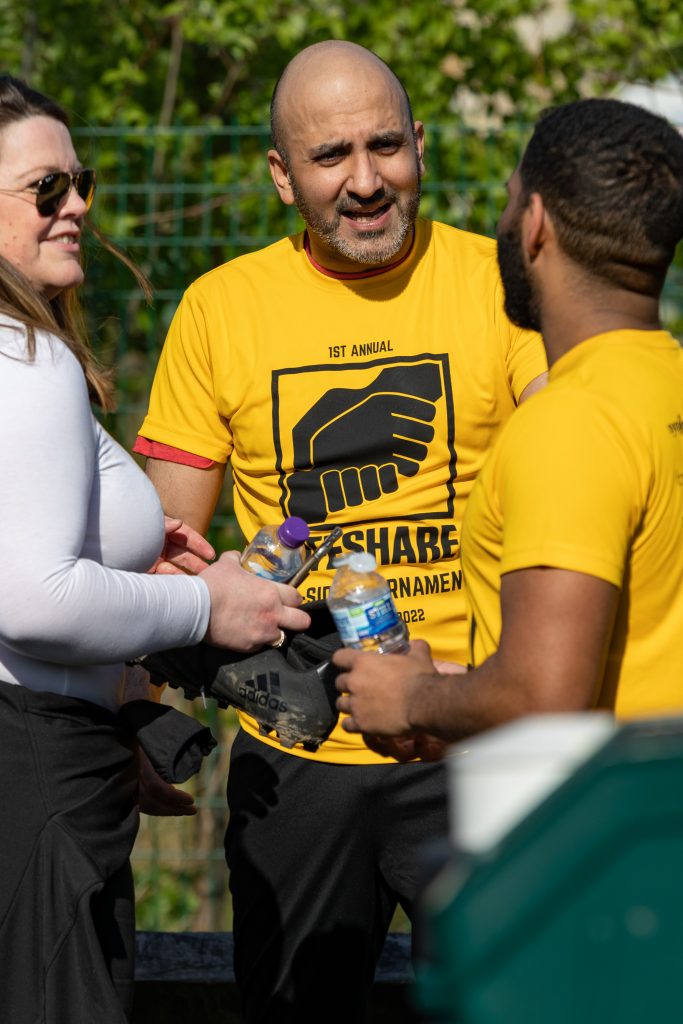 players and supporters chatting wearing yellow Lifeshare charity football tournament shirts